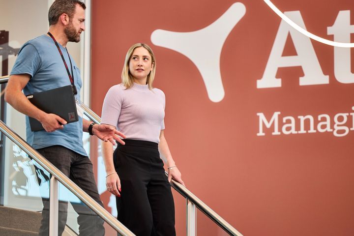 To kolleger går ned ad trappen foran et virksomhedslogo.